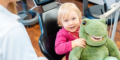 Cute toddler sitting on a dentist chair with a dinosaur doll.